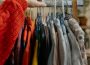 An arm in a red sleeve reaching for a piece of clothing among a rack of various clothing items.
