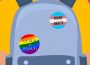 A person in a yellow shirt stands against a pink background. They’re wearing a grey backpack with three pins: one rainbow-striped heart, one rainbow-striped circle with the words “QUEER & PROUD,” and a circle with the colours of the trans flag that says “TRANS RIGHTS.”