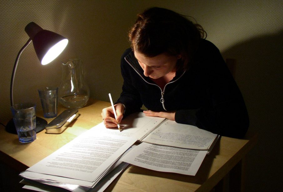 A person at a desk, studying by the light of a desk lamp.