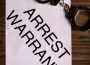 A pair of handcuffs lie on top of a paper that reads “ARREST WARRANT”
