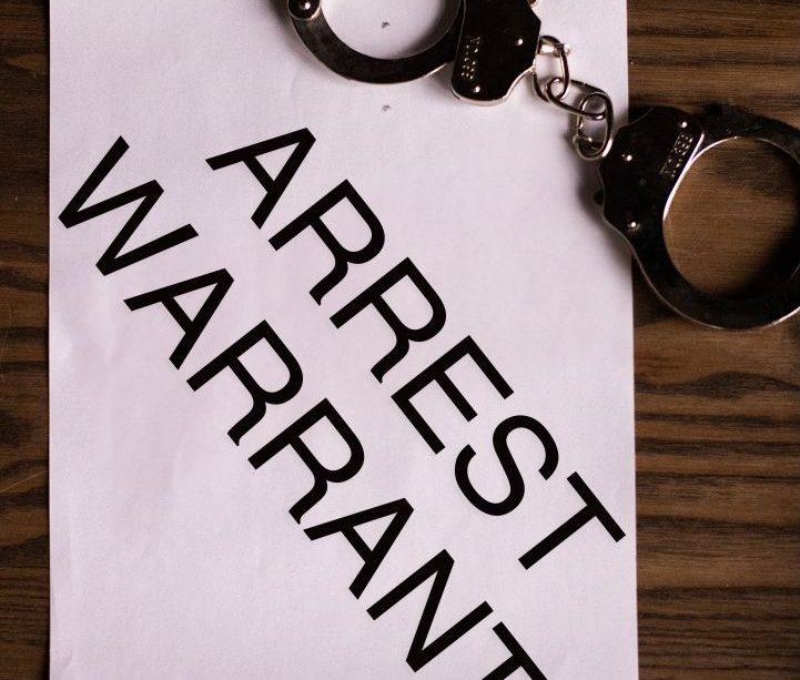 A pair of handcuffs lie on top of a paper that reads “ARREST WARRANT”