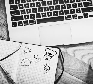 A sketch of an open notebook with doodles, resting on a laptop.