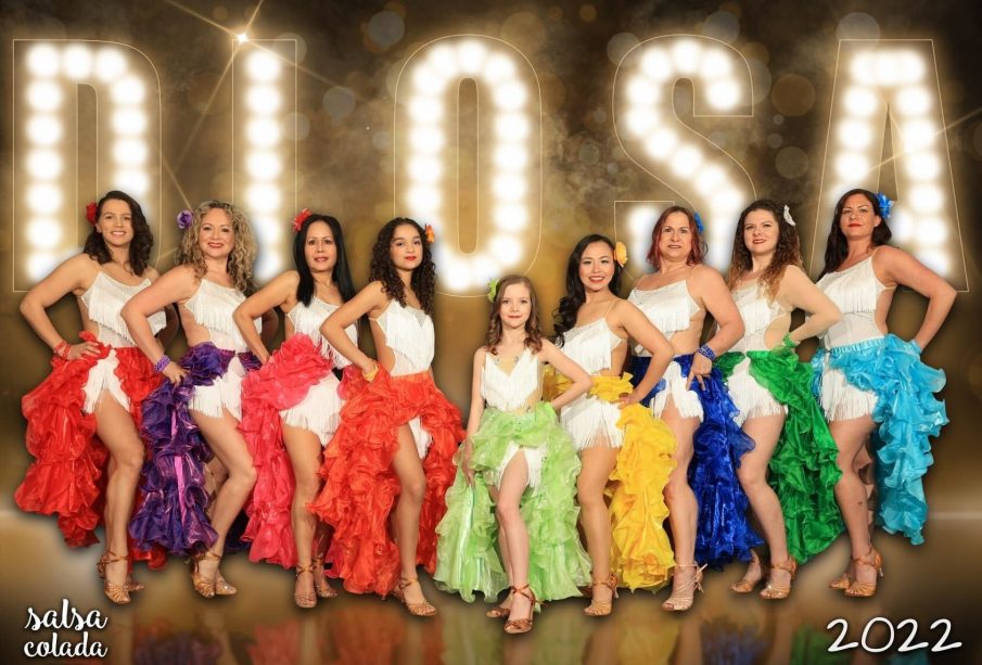 Salsa dancers lined up in front of a sign that says “DIOSA”.