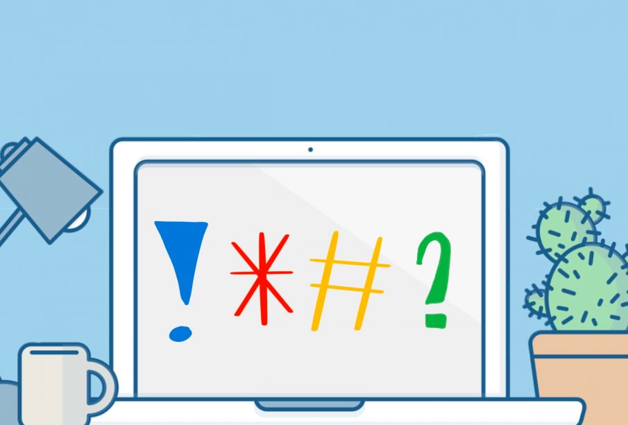 A laptop screen faces toward the viewer with an exclamation mark, asterisk, hashtag, and question mark on the screen. A task lamp, coffee mug, and cactus plant in a pot sit nearby on the desktop.