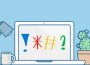 A laptop screen faces toward the viewer with an exclamation mark, asterisk, hashtag, and question mark on the screen. A task lamp, coffee mug, and cactus plant in a pot sit nearby on the desktop.