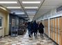 A group of students walk away from the camera through a hallway in the Education building. A Carillon newsstand is in the left corner.