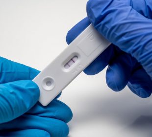 A positive COVID-19 test held in two blue-gloved hands.
