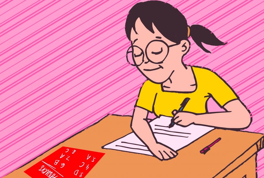 A student taking a paper exam with a red answer sheet on their desk. 