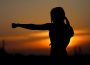 A solid black silhouette of a figure practicing a punch in a wide-open space. In the background is a sunset.