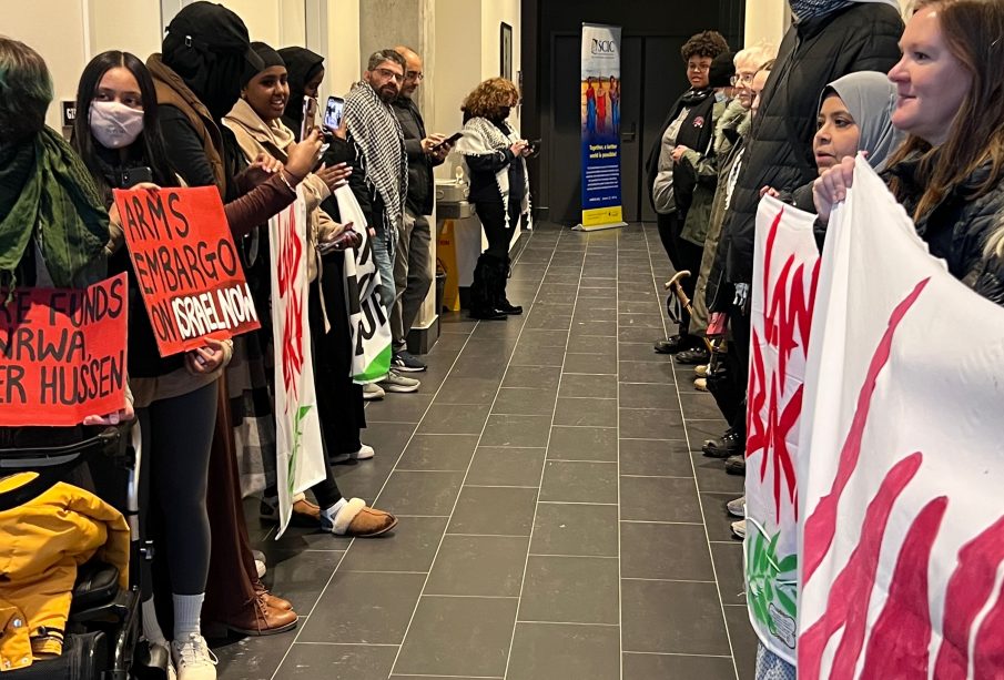 Two rows of protestors for Palestine line either side of a hallway. 