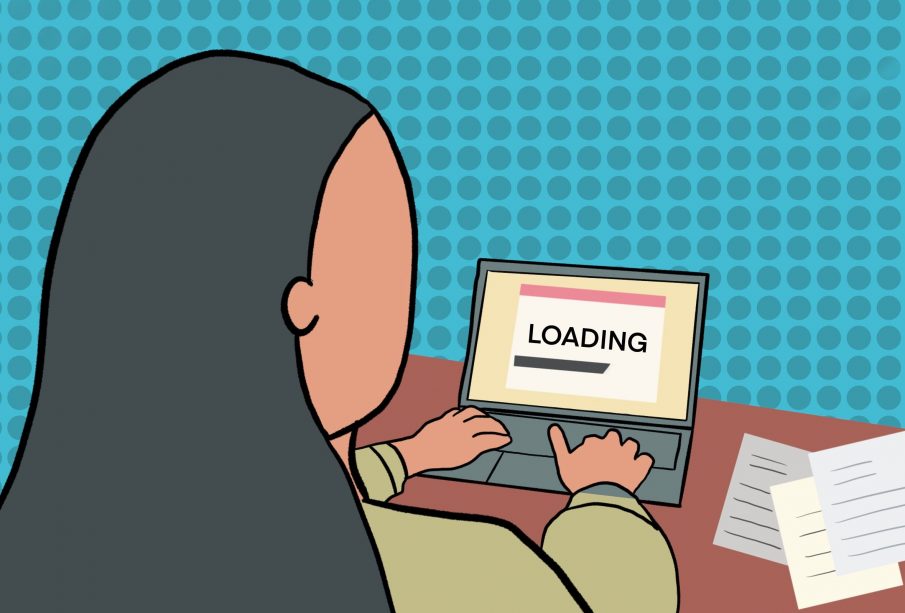 A person with long grey hair sits in front of an open laptop displaying a loading page. The person is wearing a light green sweater and has their hands on the keyboard.