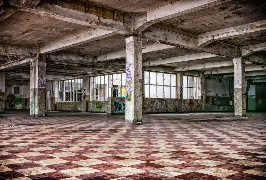 An abandoned building sits empty. Graffiti can be seen inside of it, and paint is peeling off of the ceiling.