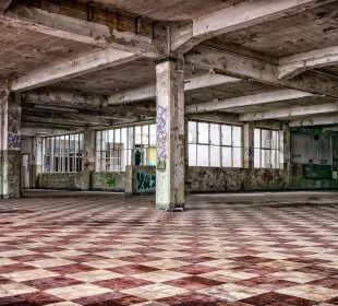 An abandoned building sits empty. Graffiti can be seen inside of it, and paint is peeling off of the ceiling. 