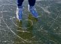 A photo of someone standing on ice in ice skates. The ice is scratched up and may be a frozen lake. Only the person’s skates and jeans are visible.
