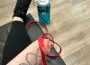 A photo of shae sackman holding a red resistance band. A blue water bottle is on the floor, and sackman sits on a black mat.