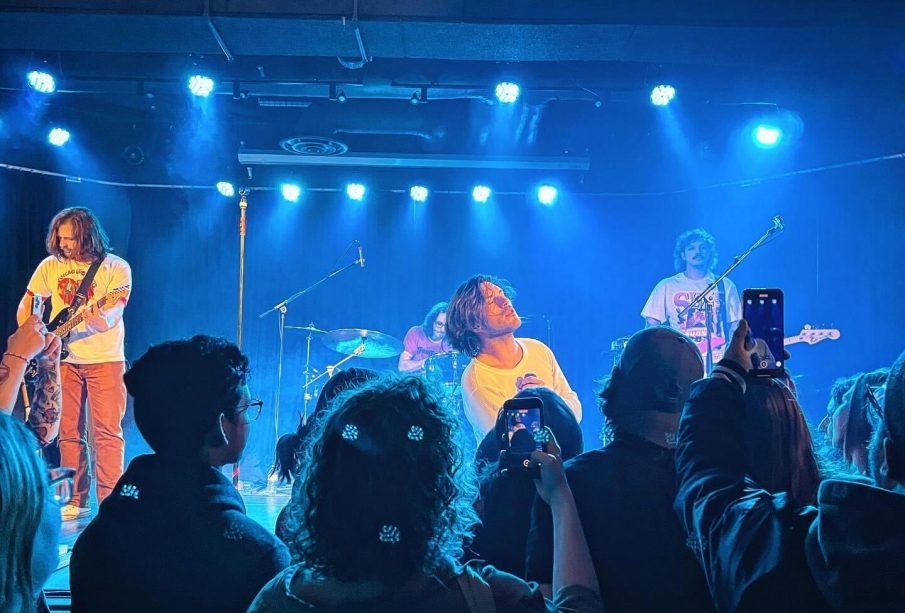 A photograph of Hotel Mira performing at Louis' in Saskatoon on February 1, 2024. The photo was taken in the section closest to the stage where people stand to watch the show, and there are other show attendees also taking photos or videos in the shot.
