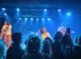 A photograph of Hotel Mira performing at Louis' in Saskatoon on February 1, 2024. The photo was taken in the section closest to the stage where people stand to watch the show, and there are other show attendees also taking photos or videos in the shot.