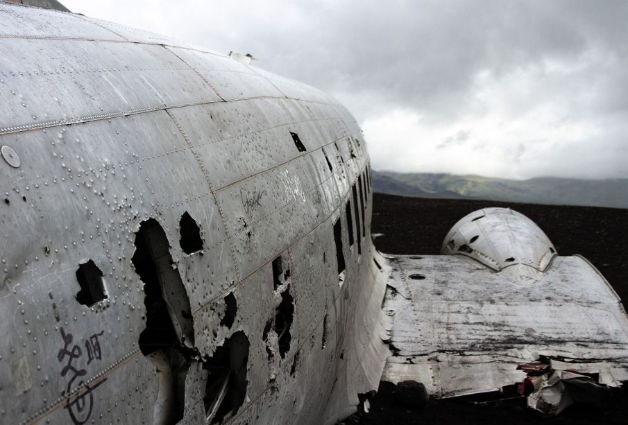 A photograph of a crashed plane. The plane is damaged and abandoned, there is nothing around for miles except a mountain range in the background.