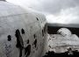 A photograph of a crashed plane. The plane is damaged and abandoned, there is nothing around for miles except a mountain range in the background.