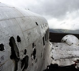 A photograph of a crashed plane. The plane is damaged and abandoned, there is nothing around for miles except a mountain range in the background.