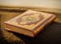 A copy of the Quran sits on a carpet and is illuminated by sunlight