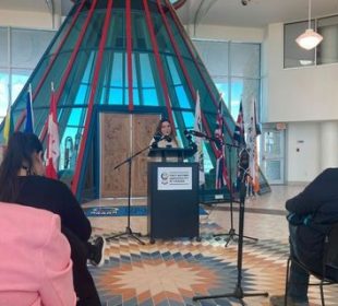 A photo is taken from the third row of the INCA announcement at FNUniv. FNUniv student Brittany Poitras makes a statement on the main floor of the university.