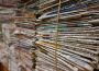 A photograph of multiple stacks of newspapers that are held together by a thin but sturdy rope.