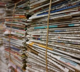 A photograph of multiple stacks of newspapers that are held together by a thin but sturdy rope.