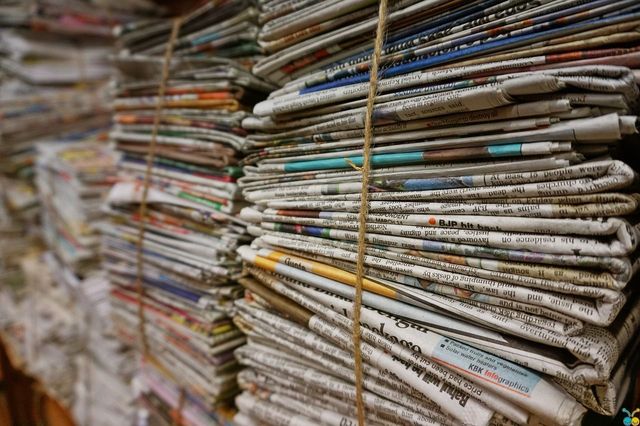A photograph of multiple stacks of newspapers that are held together by a thin but sturdy rope.