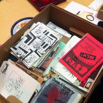 A cardboard box filled with books, pamphlets, and zines of all colours.