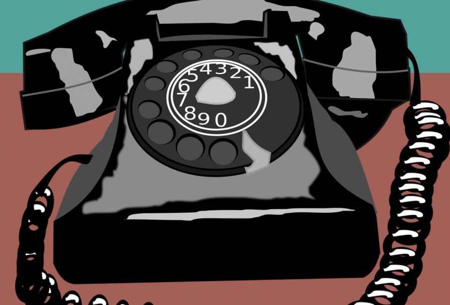 A black rotary dial telephone sits on a table with the Canadian Human Trafficking Hotline’s phone number (1-833-900-1010) above it.