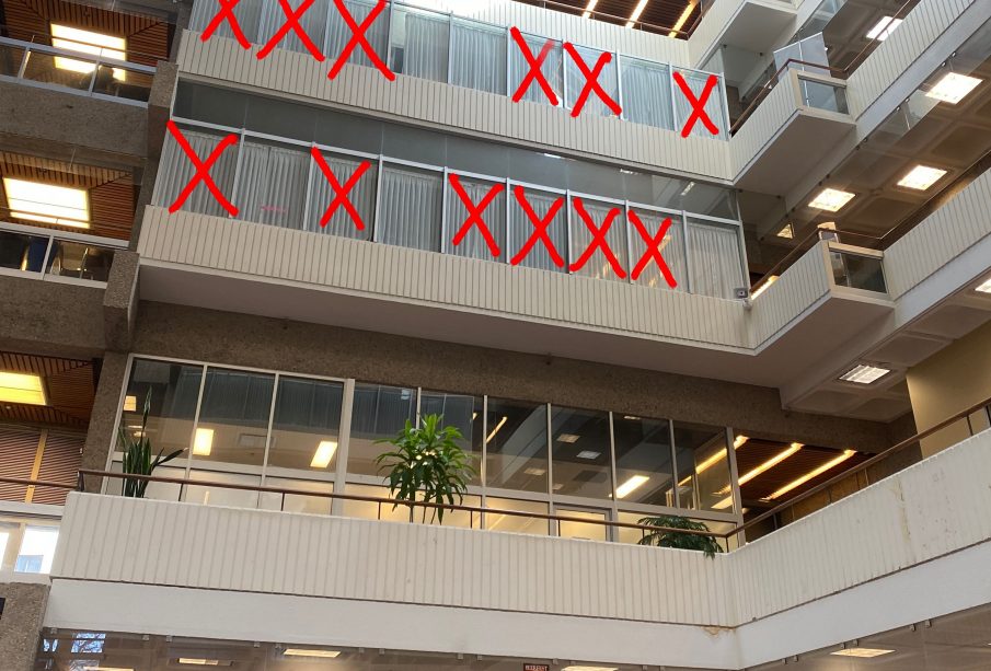 The windows of second, third, and fourth floor faculty offices in the Administration-Humanities building are seen from below. Large red “X”s cross out many of the offices 