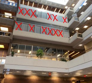 The windows of second, third, and fourth floor faculty offices in the Administration-Humanities building are seen from below. Large red “X”s cross out many of the offices 