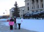Three people standing with signs/placards at an STF rally in front of the legislative building.