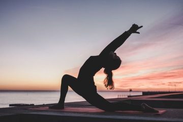 A photo of a person doing yoga outdoors by a lake.