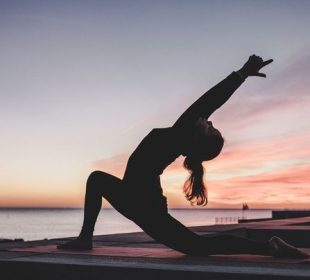 A photo of a person doing yoga outdoors by a lake.