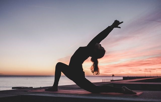 A photo of a person doing yoga outdoors by a lake.