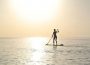 A photo of a person paddleboarding far out into the water, the sun nearing the horizon and no land in sight.