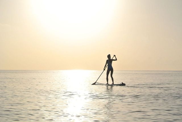 A photo of a person paddleboarding far out into the water, the sun nearing the horizon and no land in sight.