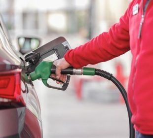 A person’s arm is shown filling up a car tank with fuel.