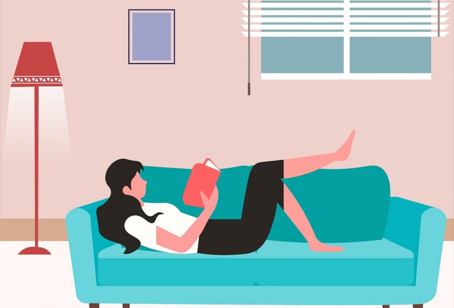 A person lying on a couch, reading a book.