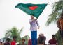 A person in blue pants holds Bangladesh’s flag. People can be seen in the background behind the person waving the country’s green and red flag