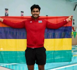 A photo of Ovesh Purahoo holding a flag of his country, Mauritius. He is standing in front of the U of R pool.