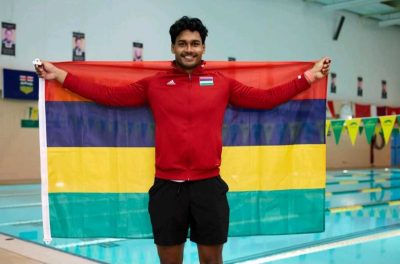 A photo of Ovesh Purahoo holding a flag of his country, Mauritius. He is standing in front of the U of R pool.