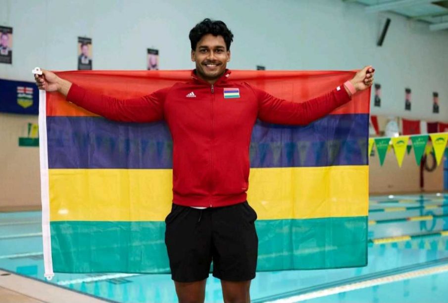 A photo of Ovesh Purahoo holding a flag of his country, Mauritius. He is standing in front of the U of R pool.