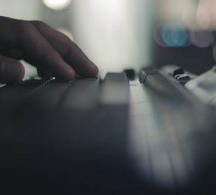 A hand rests atop a black keyboard. The foreground and background are both out of focus.
