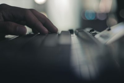 A hand rests atop a black keyboard. The foreground and background are both out of focus.