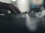 A hand rests atop a black keyboard. The foreground and background are both out of focus.