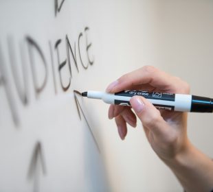 A whiteboard, with a hand holding a marker writing the word “audience.”