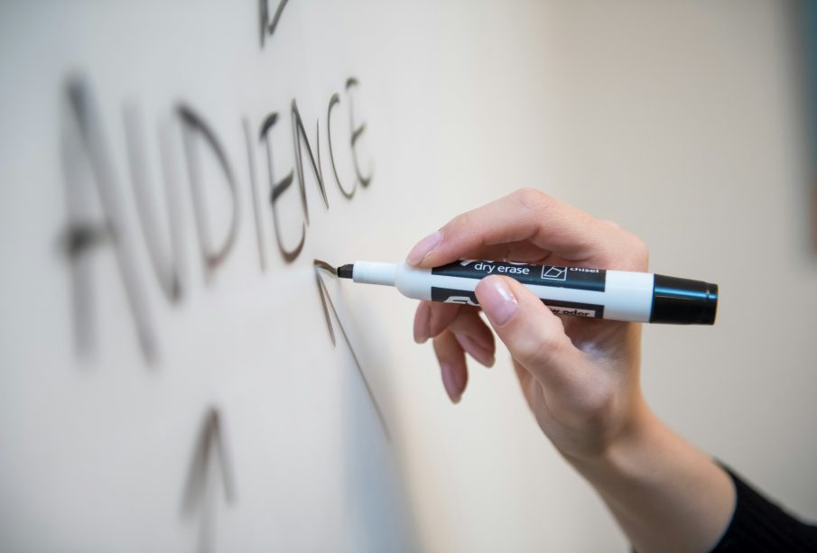 A whiteboard, with a hand holding a marker writing the word “audience.”